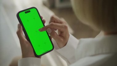 Yeşil ekran ve el kaydırmalı akıllı telefon. 60 fps içeriden krom anahtarı olan akıllı telefon kullanan bir kadın omuz manzaralı.