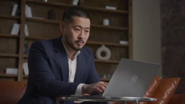 İşadamı işine odaklandı, takım elbiseli adam ofiste dizüstü bilgisayarla yazı yazıyor.