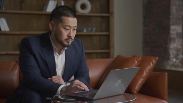 アジア人男性スーツオンラインで閲覧ラップトップを使用して ビジネスマンはロフトオフィスでコンピュータ上でインターネットをサーフィン — ストック動画