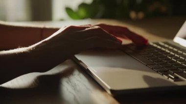 Eller dizüstü bilgisayarın dokunmatik kısmına bakıyor. Ağır çekimde, kadın kolları gün batımında yakınlaşıyor.
