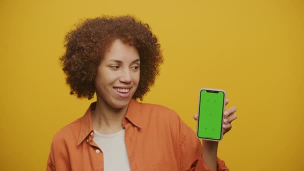 在黄色背景下手持绿色屏幕显示智能手机的女性 女性显示彩色关键智能电话的关闭 — 图库视频影像
