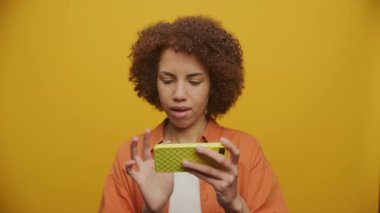 Sarı Arkaplanda 60 fps yavaş çekimde yatay akıllı telefon kullanan tatmin olmuş kadın.