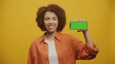 Sarı Arkaplanda Yatay Yeşil Ekran Akıllı Telefonu Tutan Kadın, Krom tuşlu akıllı telefon gösteren modern kadın