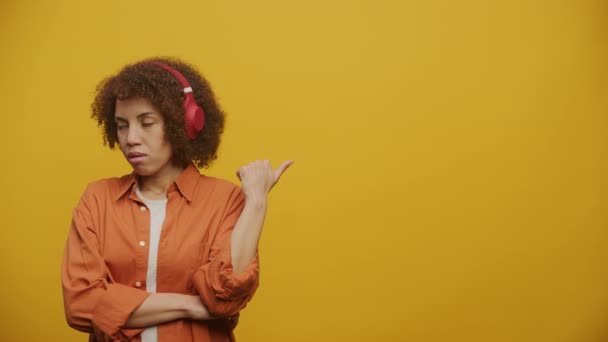 Nieszczęśliwa Kobieta Słuchawkach Wskazując Kopiuj Przestrzeń Żółtym Tle — Wideo stockowe