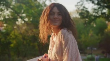 Curly woman in romantic memories from past. Young female in joy outside during sunset in slow motion
