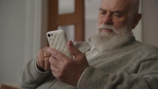スマートフォンでシニアマンブラウジング おじいちゃんはスマートフォンを保持ローアングルを閉じる — ストック動画