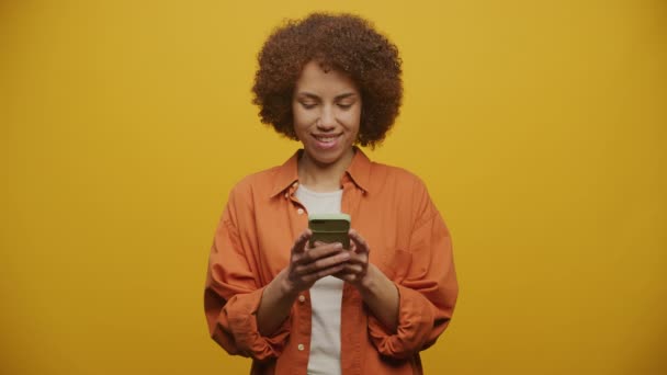 在智能手机上输入黄色背景的兴奋女性 使用智能手机和微笑的女性 — 图库视频影像