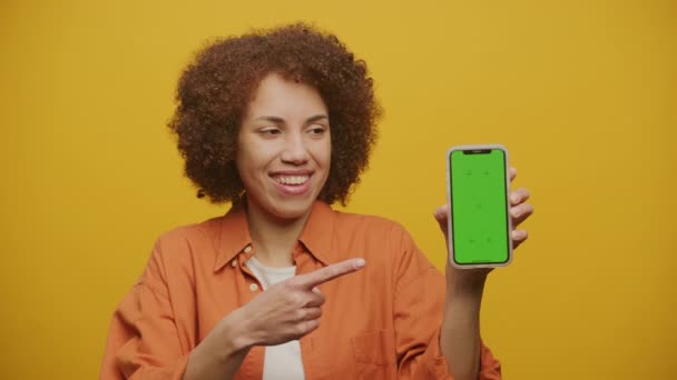 在黄色背景的Chroma Key Smartphone上指向手指的女人 — 图库视频影像