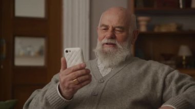 Büyükbaba video konuşmasında Smartphone kullanıyor, kıdemli adam akıllı telefondan ailesiyle konuşuyor.