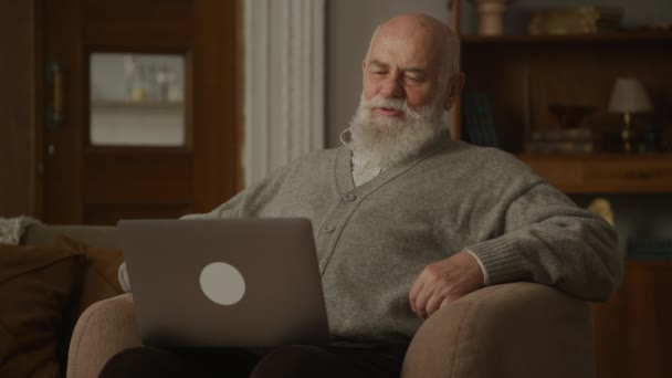 年长男子在电视交谈使用笔记本电脑 祖父在扶手椅说话 — 图库视频影像