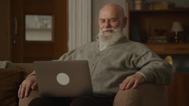 ビデオ通話で話すシニア男性ラップトップを使用して 肘掛け椅子で祖父話す — ストック動画