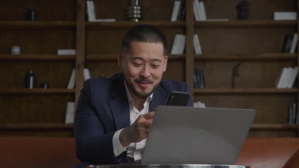 会議中の男ノートパソコンで働くスマートフォンを使用してオフィスでのビデオ通話 — ストック動画