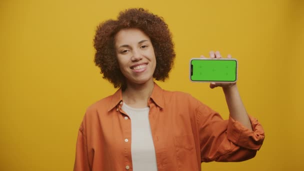 黄色背景下的女性手持水平绿色屏幕智能手机 女性显示彩色密钥智能电话 — 图库视频影像