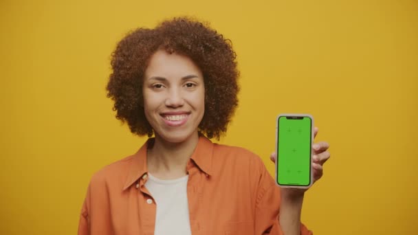 黄色背景下的女性手持彩色密钥智能手机 女性显示绿色屏幕智能手机关闭 — 图库视频影像