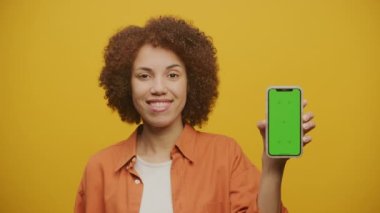 Woman Showing Green Screen Smart Phone on Yellow Background, Female Holding Chroma Key Smartphone