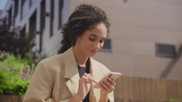 女人在智能手机上边浏览边笑 女商人在商务中心公园用智能手机 — 图库视频影像