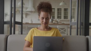 Apartmandaki koltukta oturan dizüstü bilgisayarlı kadın, Bilgisayarda çalışan pozitif kadın.