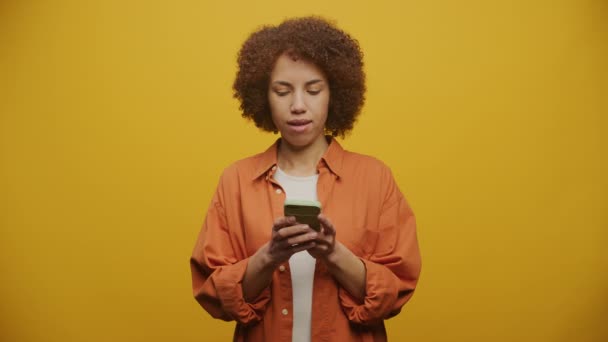 在黄色背景下在智能手机上发笑的女人 — 图库视频影像