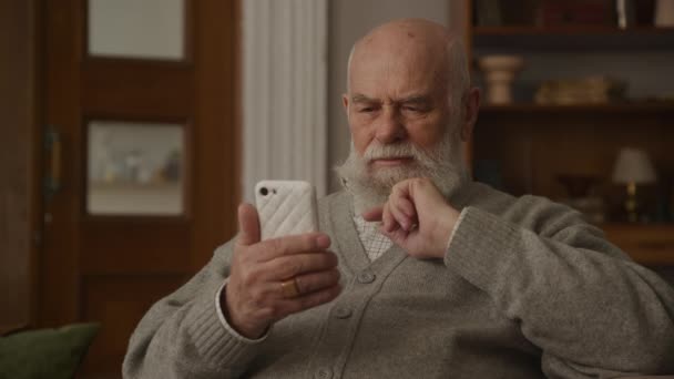 心烦意乱的祖父在智能手机上读到一则信息 情绪化的老人收到了坏消息 — 图库视频影像