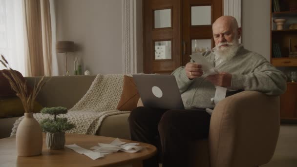 Älterer Mann Blättert Wohnzimmer Rechnungen Durch Großvater Verwaltet Mit Laptop — Stockvideo