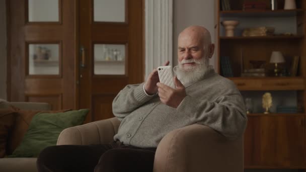 Senior Man Reading Smartphone Laughing Armchair Παππούς Περιήγηση Απευθείας Σύνδεση — Αρχείο Βίντεο