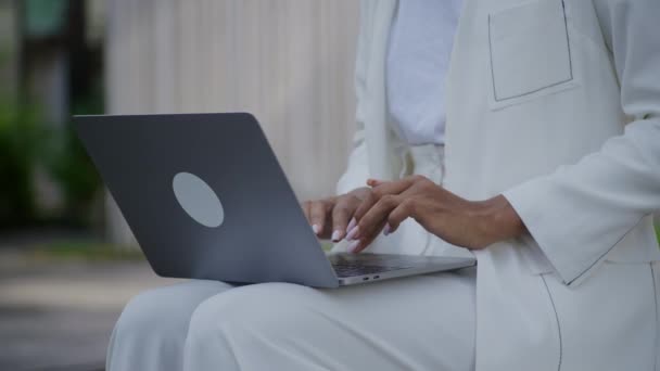 ラップトップのキーボードでタイピングする女性の手の周りを周回する 屋外で閉じる 彼女の膝にコンピュータを使用している女性 — ストック動画