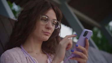 Çevrimiçi Kıvırcık Kadın Parkta Mor Akıllı Telefon Kullanıyor, Gözlüklü Kadın Açık havada Sörf Yapıyor