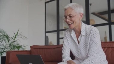 Evde Dizüstü bilgisayardan iyi haberler okuyan olgun bir kadın, Kıdemli Yetişkin Kadın Başarı Kutlaması