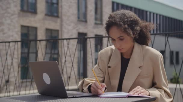 オンラインクラスの屋外でのノートブックでの学生の執筆 外でラップトップを使用してノートを作る女性 — ストック動画