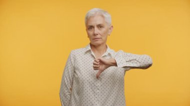Olgun Kadın Sarı Arkaplanda Hoşnutsuzluk Gösteriyor, Kıdemli Yetişkin Kadın Başparmağı Aşağı İşareti
