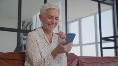 Kıdemli Kadın Ofiste Akıllı Telefon 'da İyi Haberler Okuyor, Yetişkin Bayan Başarı Kutlaması