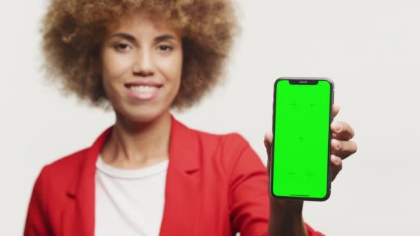 身穿红色西装 手持绿色屏幕智能手机 背景为白色 卷曲的女商人展示了Chroma键智能手机的女性 — 图库视频影像