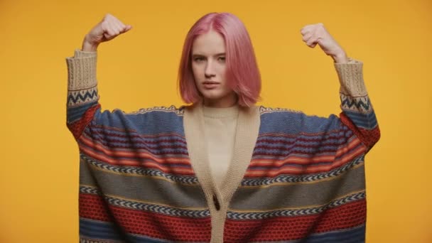 イエローバックグラウンドで強度ジェスチャーを示す女性 パワーサインで腕を上げるピンクの髪の学生 — ストック動画
