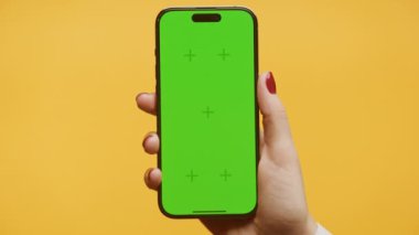 Sarı Arkaplanda Yavaş Optik Yakınlaştır Yeşil Ekran Akıllı Telefonu, Krom Elli Kadın Akıllı Telefonu