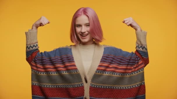 イエローバックグラウンドで強度ジェスチャーを表示する学生 パワーサインで腕を上げるピンクの髪の女性 — ストック動画