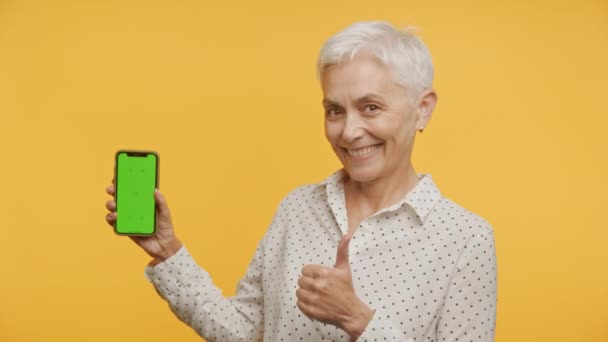 Gammal Kvinna Som Gesture Holding Grön Skärm Smartphone Gul Bakgrund — Stockvideo