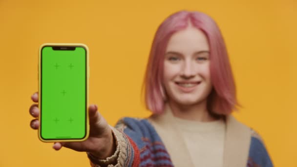 持有绿色屏风智能手机的女性关注黄色背景 粉色头发的年轻女士展示垂直色谱关键智能手机 — 图库视频影像