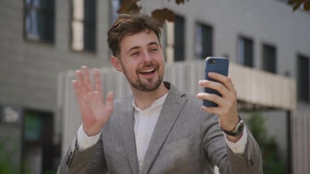 オフィスファシリティパークでスマートフォンアウトドアを使用してビデオ通話でビジネスマン挨拶ジェスチャー — ストック動画
