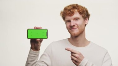 Ginger Man Point at Green Screen Smartphone on White Background, Kızıl saçlı adam Chroma Key Smart Phone gösteriyor