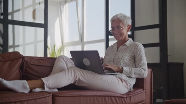 Mosolygó Senior Woman Gépelés Laptop Kanapén Beltéri — Stock videók