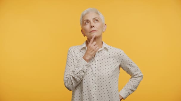 黄色の背景で好奇心旺盛な決断を検討する熟練した高齢女性 — ストック動画