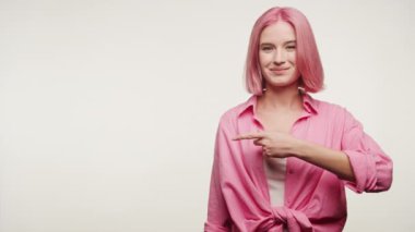Pembe saçlı, gülümseyen genç bir kadın, açık arkaplanda günlük pembe bir gömlek giyiyor.