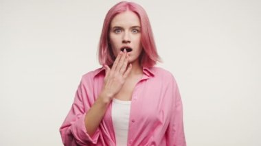 Pembe saçlı bir kadın şaşkınlığını ifade ediyor, beyaz bir arka plana karşı eliyle ağzını kapatıyor.