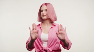 Pembe saçlı genç bir kadın elleriyle dur işareti yapıyor, sınır işareti yapıyor ya da beyaz arka planda reddediyor.
