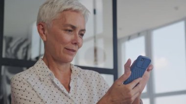 Kısa saçlı neşeli, olgun bir kadın. İçerideki akıllı telefona bakarken gülüyor.