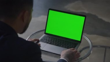 Modern çalışma alanında krom ekranlı dizüstü bilgisayar kullanan profesyonel takım elbiseli, omuzlarının üstünden görülüyor.