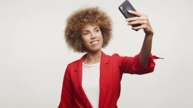 Kırmızı ceketli neşeli bir kadın, beyaz arka plandaki modern bağlılık ruhunu somutlaştıran selfie ile mutlu bir anı yakalar.