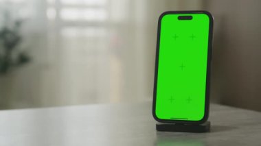 Yükleme limanında duran akıllı telefon içerik değişimine hazır yeşil bir ekranla modern bir masaya yerleştirildi.