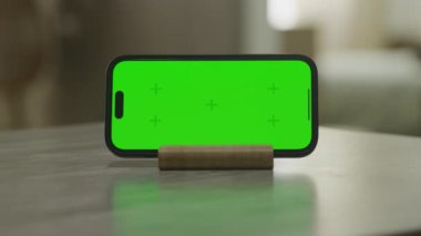 Basit bir tutucu üzerinde yatay akıllı telefon kolay içerik değişimi için canlı yeşil bir ekran, nötr bir yüzey üzerine ayarlı
