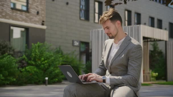 Jovem Vestido Terno Negócios Trabalha Atentamente Laptop Enquanto Sentado Livre — Vídeo de Stock